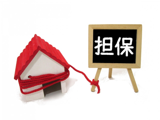 家の模型と担保と書かれたカードを赤い糸で結び付けている写真